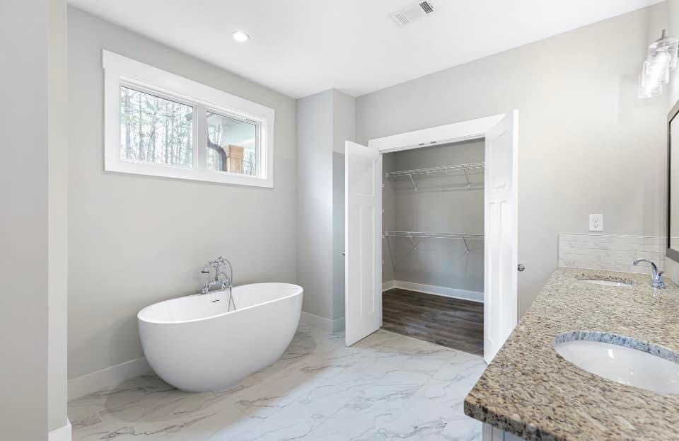 Spacious modern bathroom with a freestanding soaking tub, double granite vanity, and walk-in closet in a new construction home.