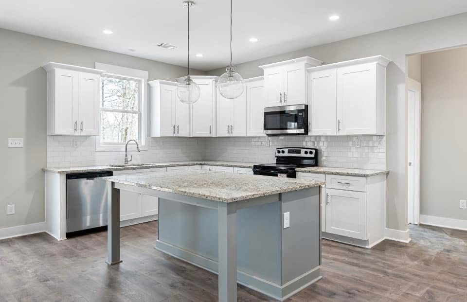 Modern kitchen with white shaker cabinets, granite countertops, stainless steel appliances, and a large island in a new custom home.